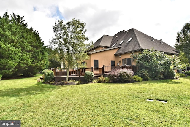rear view of property featuring a shingled roof, stucco siding, a deck, and a yard