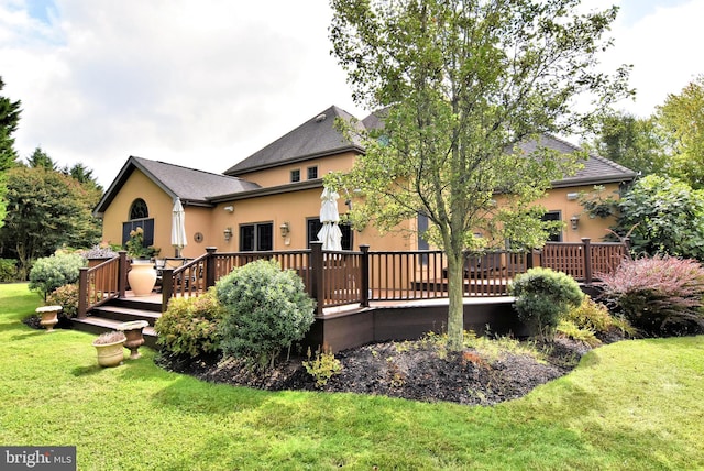 rear view of property featuring stucco siding, a wooden deck, and a yard