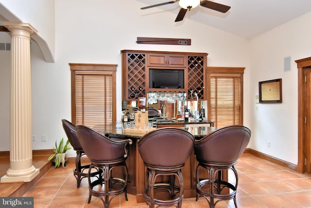 bar featuring vaulted ceiling, decorative columns, wet bar, light tile patterned floors, and a ceiling fan