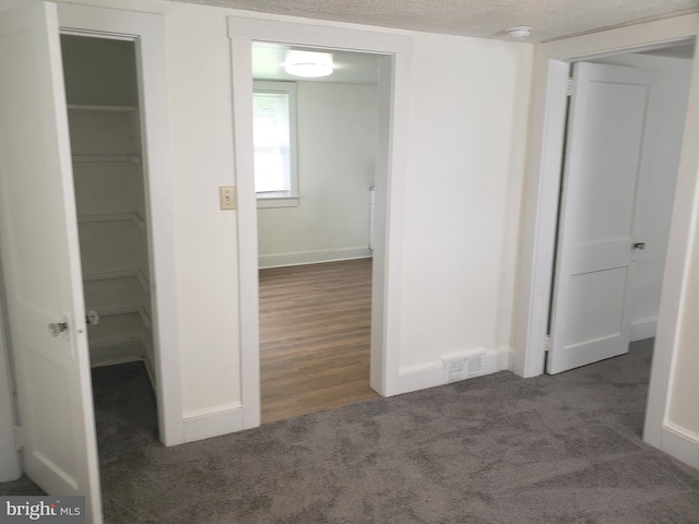 hallway with dark carpet and a textured ceiling