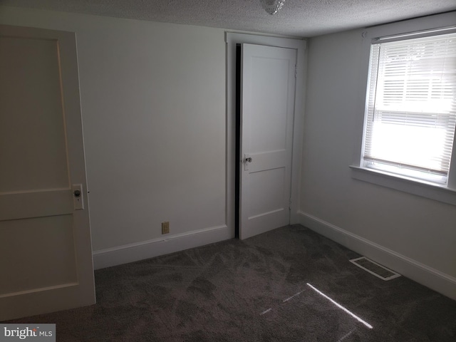 spare room with a textured ceiling, dark colored carpet, and plenty of natural light