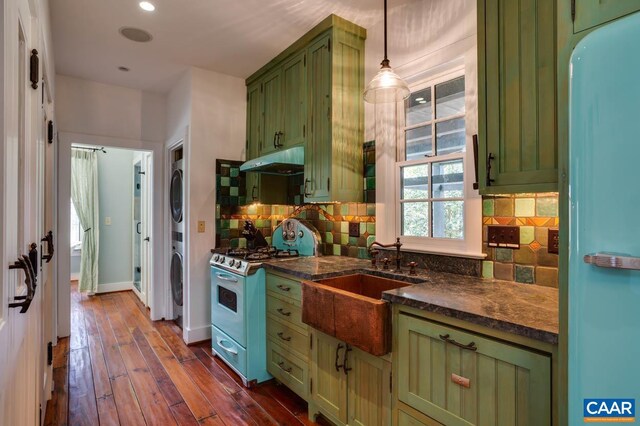 kitchen featuring dark hardwood / wood-style floors, green cabinetry, stacked washing maching and dryer, white appliances, and decorative light fixtures