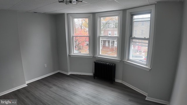 spare room featuring a drop ceiling, radiator, and dark wood-type flooring