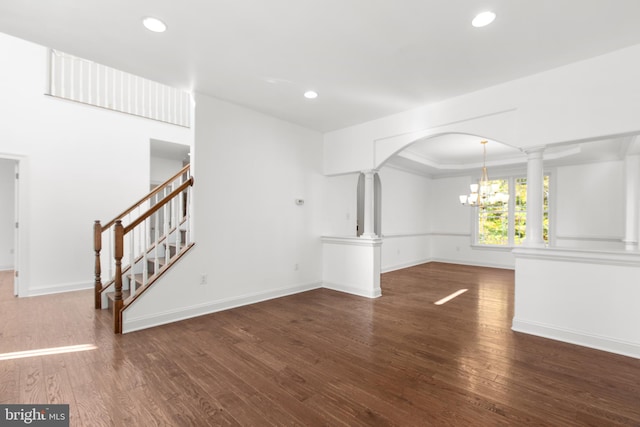 unfurnished living room with dark hardwood / wood-style floors, a notable chandelier, and decorative columns