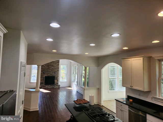 kitchen with black gas stovetop, a stone fireplace, decorative columns, dishwasher, and dark hardwood / wood-style flooring