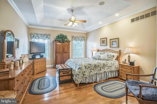 bedroom with light wood-type flooring, multiple windows, a raised ceiling, and ceiling fan