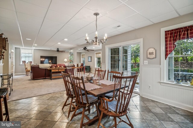 carpeted dining room with ceiling fan with notable chandelier, a wealth of natural light, and a drop ceiling