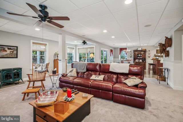 living room featuring a wood stove, ceiling fan, light colored carpet, and a healthy amount of sunlight