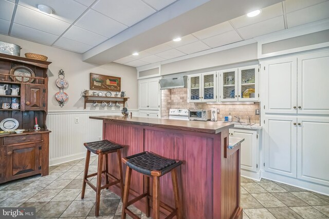 kitchen with white cabinets, white electric range, a kitchen breakfast bar, a center island, and decorative backsplash