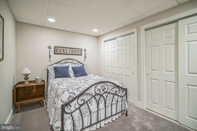 carpeted bedroom with a paneled ceiling and multiple closets