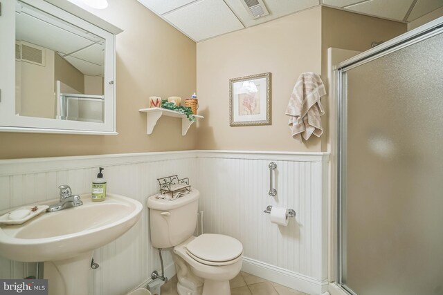 bathroom with a paneled ceiling, toilet, tile patterned floors, and a shower with shower door