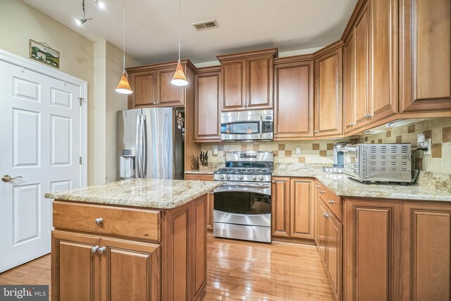 kitchen with decorative backsplash, a kitchen island, pendant lighting, stainless steel appliances, and light hardwood / wood-style flooring