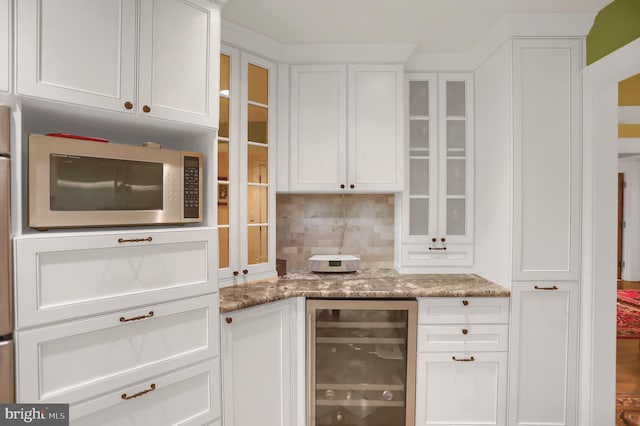 kitchen with wine cooler, white cabinetry, glass insert cabinets, stainless steel microwave, and decorative backsplash