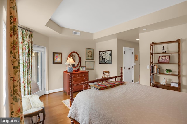 bedroom with a tray ceiling, baseboards, access to exterior, visible vents, and wood finished floors