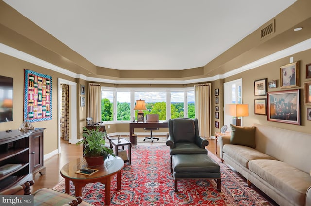 living area featuring baseboards, visible vents, wood finished floors, and ornamental molding