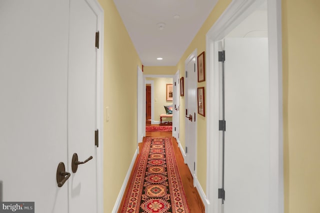 hallway featuring baseboards, wood finished floors, and recessed lighting