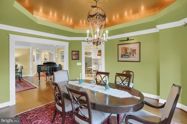 dining space featuring an inviting chandelier, a tray ceiling, crown molding, and hardwood / wood-style floors