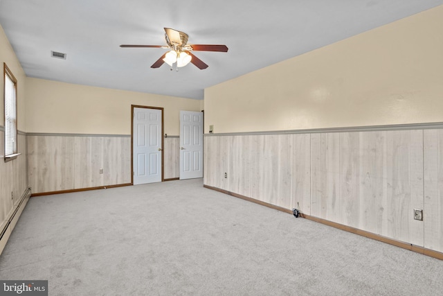 unfurnished room with light carpet, a baseboard heating unit, wood walls, and ceiling fan