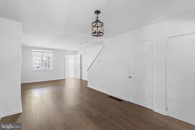 empty room featuring a notable chandelier and dark wood-type flooring