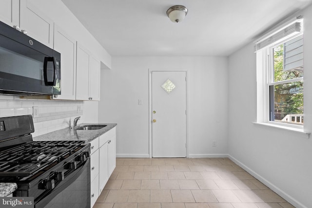 kitchen featuring light stone counters, white cabinets, black gas stove, and sink