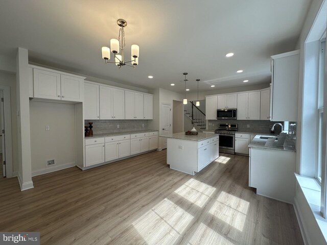 kitchen featuring stainless steel appliances, a kitchen island, pendant lighting, white cabinets, and sink