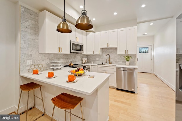 kitchen with kitchen peninsula, hanging light fixtures, a breakfast bar, sink, and appliances with stainless steel finishes