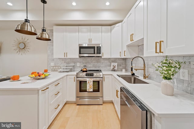 kitchen with sink, appliances with stainless steel finishes, white cabinets, and hanging light fixtures