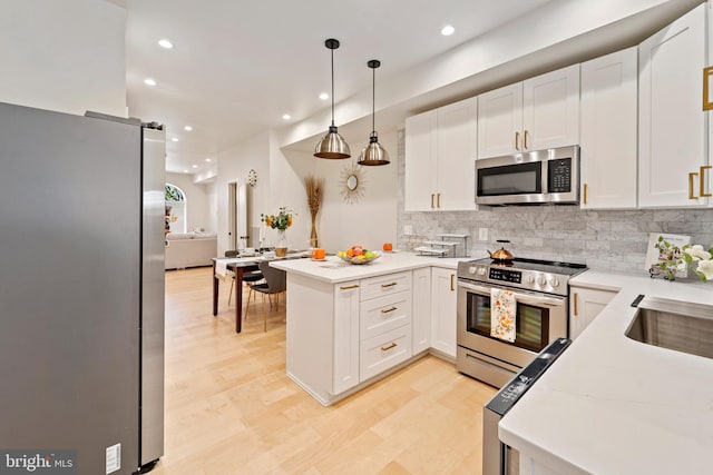 kitchen featuring white cabinetry, kitchen peninsula, hanging light fixtures, stainless steel appliances, and a barn door