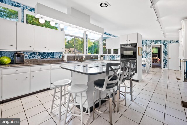 kitchen featuring white cabinets, a kitchen island, dishwasher, a breakfast bar, and decorative backsplash