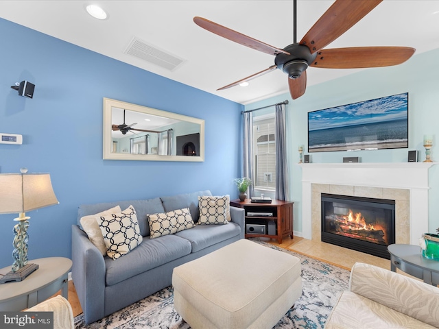 living room with a tiled fireplace and ceiling fan