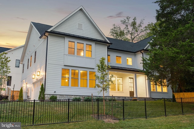 back house at dusk featuring a lawn and a garage