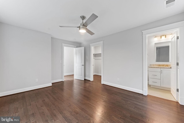 unfurnished bedroom featuring a spacious closet, dark hardwood / wood-style floors, ceiling fan, and ensuite bathroom