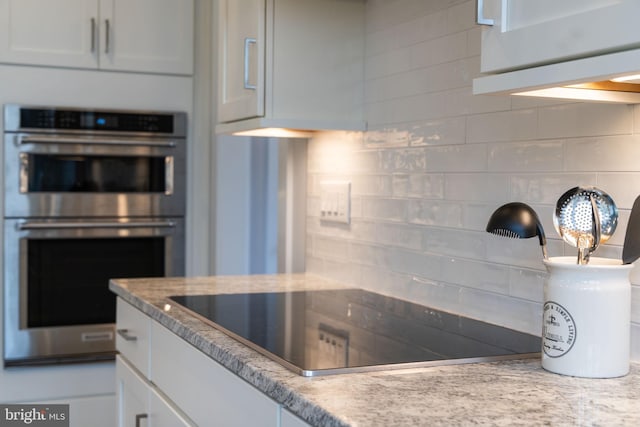 kitchen with black electric cooktop, backsplash, double oven, and white cabinets