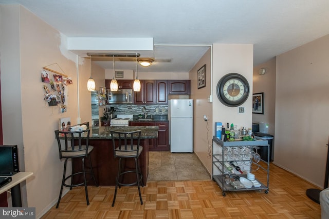 kitchen with pendant lighting, sink, white appliances, dark brown cabinets, and a breakfast bar area