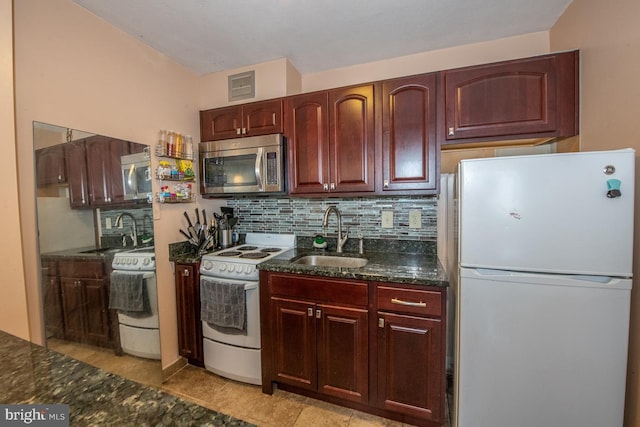 kitchen with white appliances, dark stone countertops, sink, and light tile patterned floors