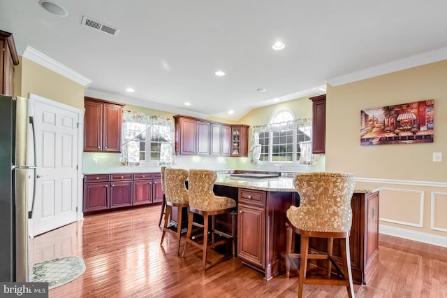 kitchen featuring a breakfast bar, a center island, stainless steel refrigerator, and crown molding