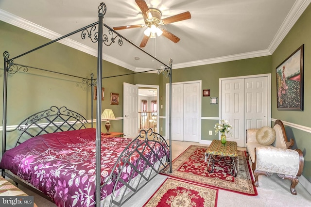 carpeted bedroom featuring ceiling fan, ornamental molding, and two closets