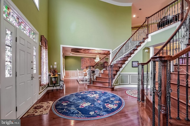 foyer with wood-type flooring, a towering ceiling, crown molding, and decorative columns