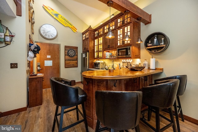 bar with stainless steel microwave, backsplash, wood counters, hardwood / wood-style floors, and lofted ceiling