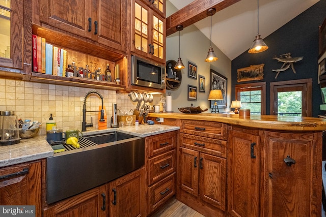 kitchen featuring stainless steel microwave, sink, backsplash, light stone counters, and light hardwood / wood-style flooring