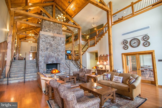 living room featuring hardwood / wood-style flooring, a chandelier, high vaulted ceiling, wooden ceiling, and a stone fireplace