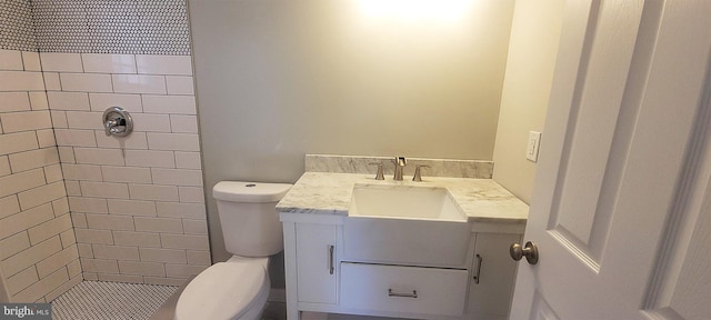 bathroom featuring a tile shower, vanity, and toilet