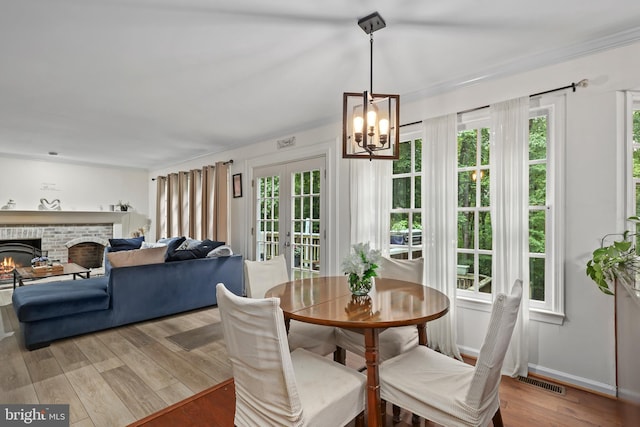 dining area with light wood-type flooring, crown molding, a fireplace, and an inviting chandelier