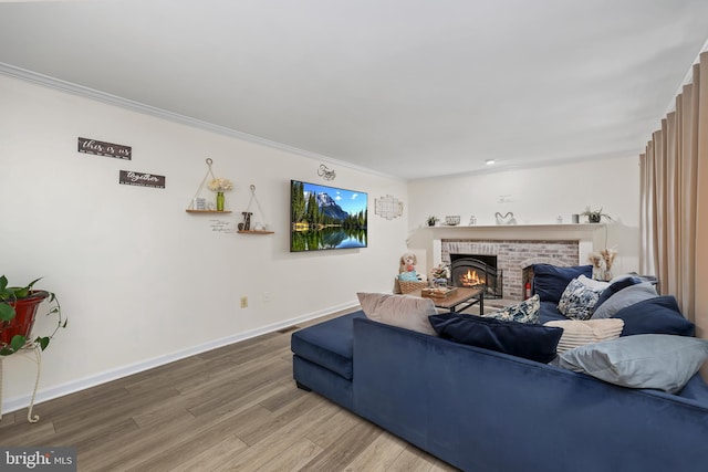 living room with wood-type flooring, ornamental molding, and a brick fireplace