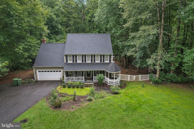 colonial home featuring a front yard, a garage, and covered porch