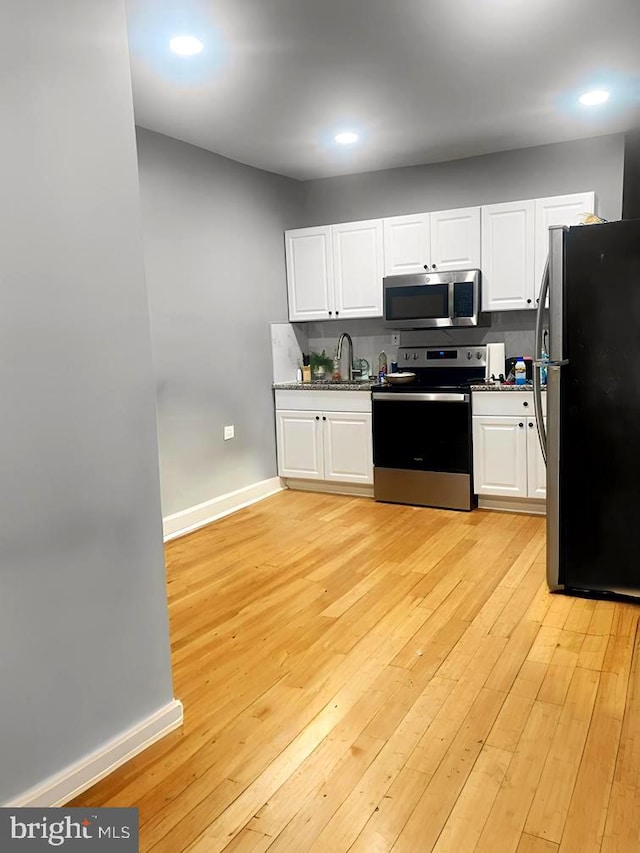 kitchen with white cabinets, backsplash, appliances with stainless steel finishes, light wood-type flooring, and sink