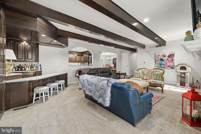 living room featuring light colored carpet, beam ceiling, and indoor bar