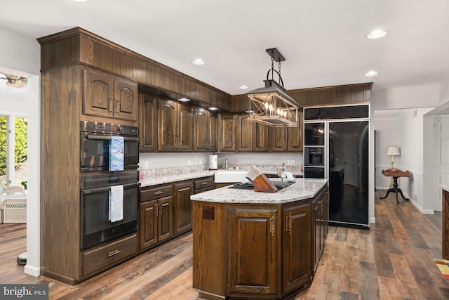 kitchen featuring a center island, hardwood / wood-style flooring, black appliances, dark brown cabinetry, and decorative light fixtures