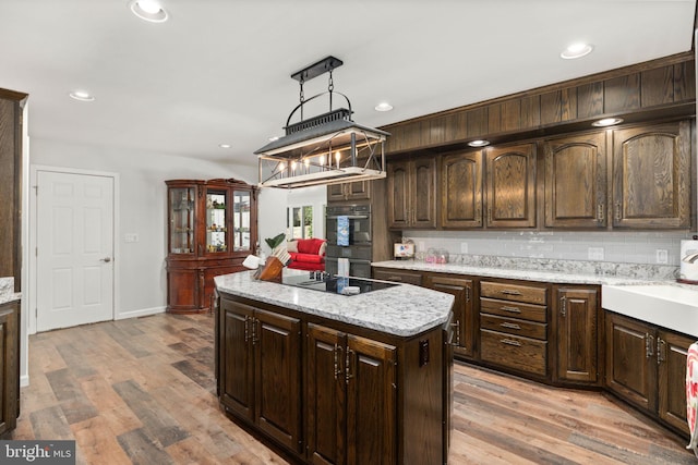 kitchen with dark brown cabinets, pendant lighting, light hardwood / wood-style floors, and tasteful backsplash