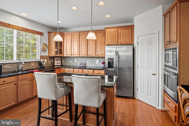 kitchen with hanging light fixtures, stainless steel appliances, sink, a center island, and light hardwood / wood-style floors